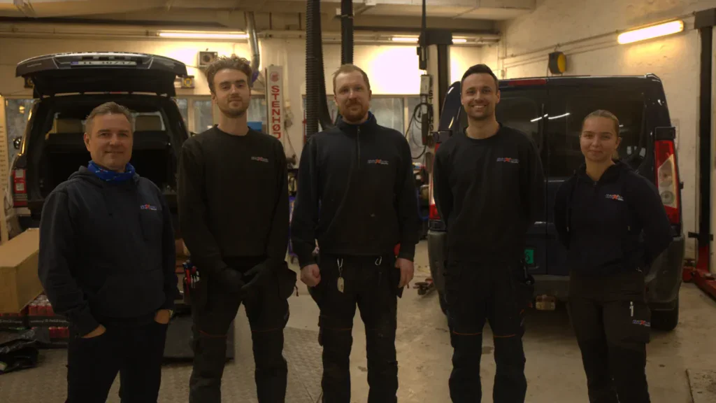 Fagfolk foran en arbeidsbil i verkstedets interiør hos Søreidebil, service og reparasjon av biler.